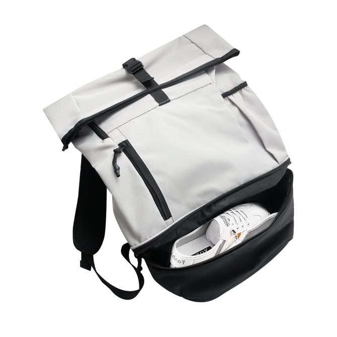 A grey and black roll-top backpack with zippered pockets, featuring a pair of white sneakers inside.