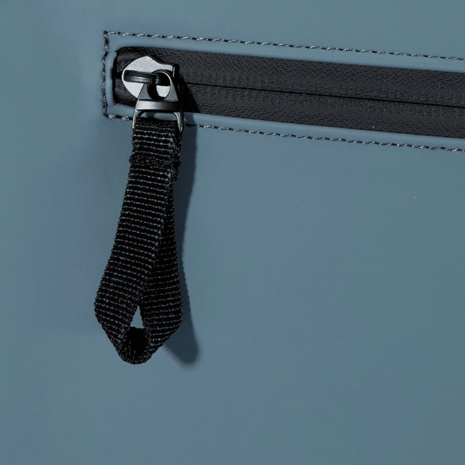 A close-up of a grey backpack's zip fastening and pull tab, featuring a black fabric loop.