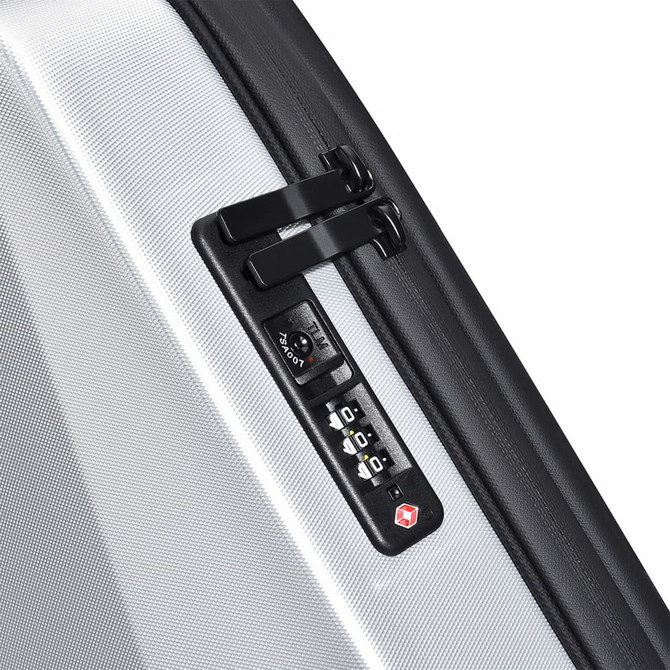 A close-up of a silver expandable hardshell backpack featuring a black zipper and a combination lock.
