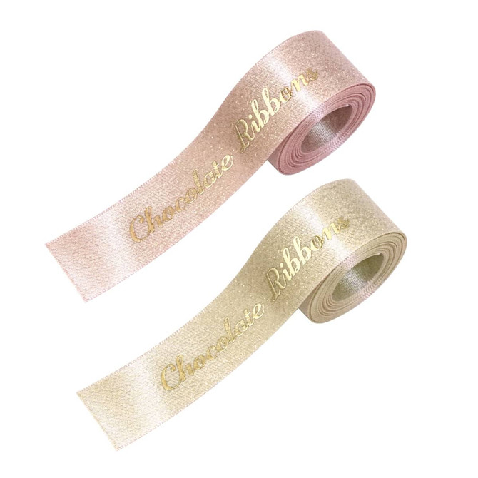 Two rolls of satin ribbon in pale pink and light gold, both with the text "Chocolate Ribbon" in gold lettering.