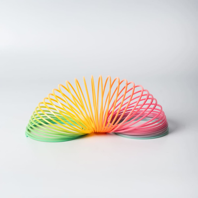A novelty rainbow slinky features vibrant yellow, pink, and green colours, showcasing a spiralled design.
