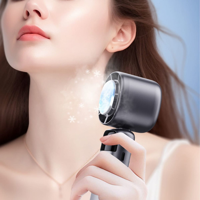 A portable cooling fan in black, held by a person, emits a gentle breeze, surrounded by sparkling effects.