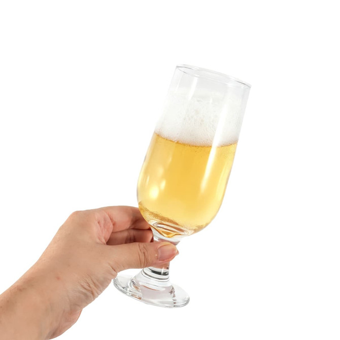 A goblet glass filled with a golden beverage and topped with foam, held in a hand. The glass has a clear design.