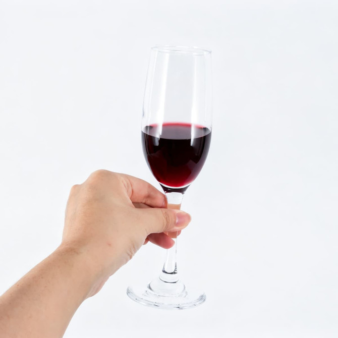 A hand holding a clear, stemmed wine glass filled with red wine against a white background.