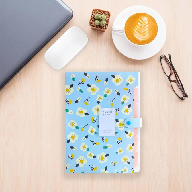 A floral-patterned expandable file folder in blue, featuring a clasp, positioned on a wooden surface with a cup of coffee and glasses.