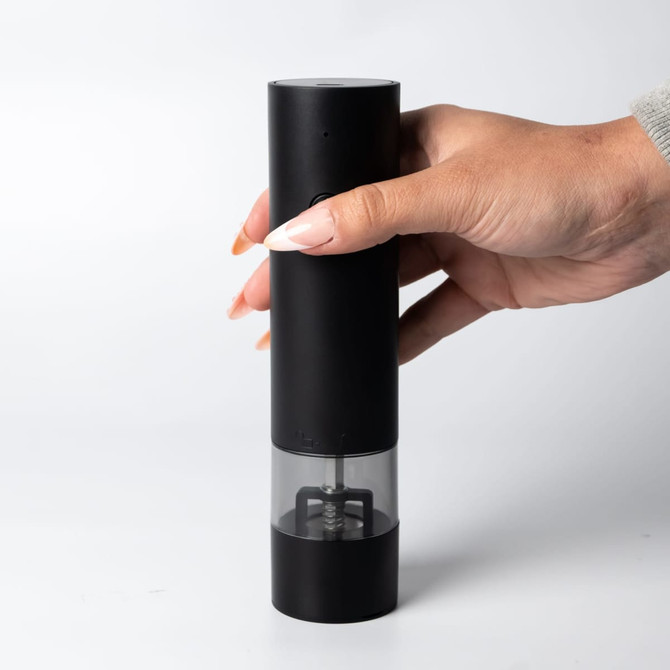 A black rechargeable pepper/salt grinder with a transparent section, held in a hand, featuring a sleek design.