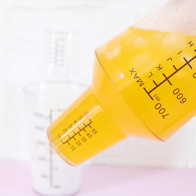 A drink bottle in orange and clear with measurement markings, featuring a measuring cap. It has a logo.