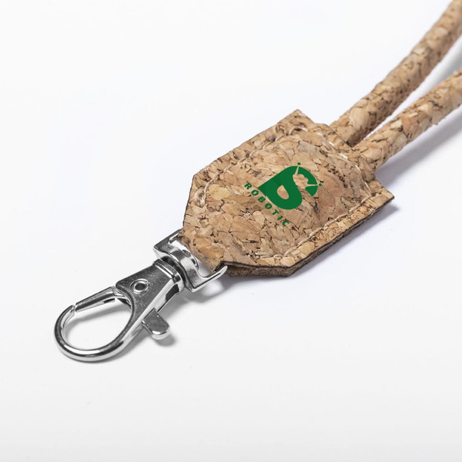 A cork lanyard featuring a metal clasp and a small branded tag in green. The natural cork texture is prominently displayed.