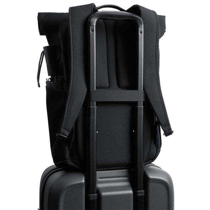A black rolltop backpack is secured on a black suitcase, featuring padded straps and a side pocket.