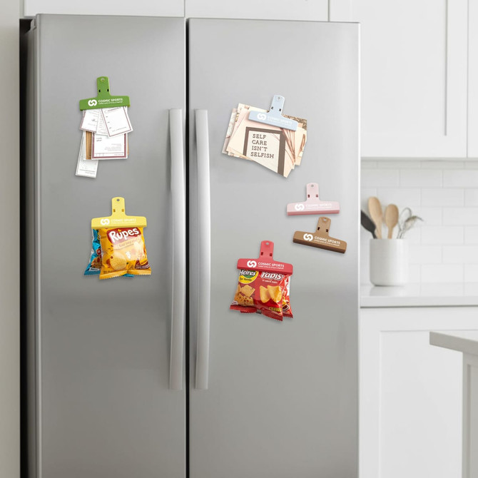 A fridge features various coloured plastic magnetic clips holding notes and snack packets. The clips include blue, pink, green, and beige.