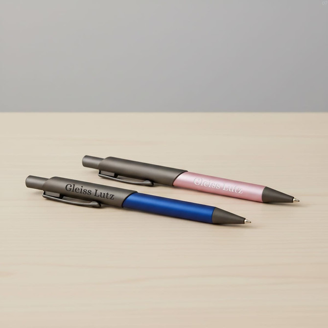 A set of two Arc Metal Pens in blue and pink, featuring a logo, resting on a wooden surface.