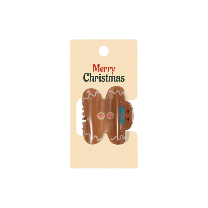 A Christmas-themed hair claw in the shape of a gingerbread man, featuring brown, pink, and blue colours on a card.
