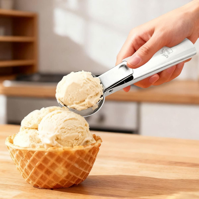 A silver ice cream scoop with a white handle is shown lifting a scoop of ice cream from a waffle cone bowl.