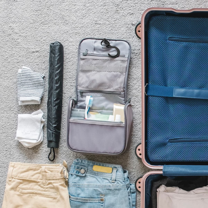 A grey hanging travel toiletry bag with compartments and contents, alongside folded clothes and an umbrella.