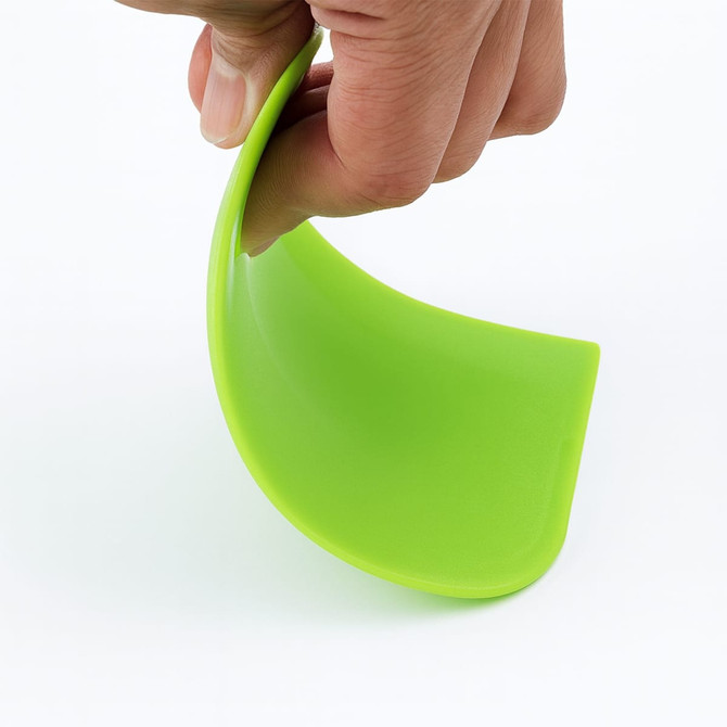 A green plastic flexible bowl scraper held by a hand, showcasing its bendable design.