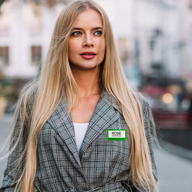 A woman with long blonde hair wears a grey checked blazer. She is outdoors in a blurred urban setting.