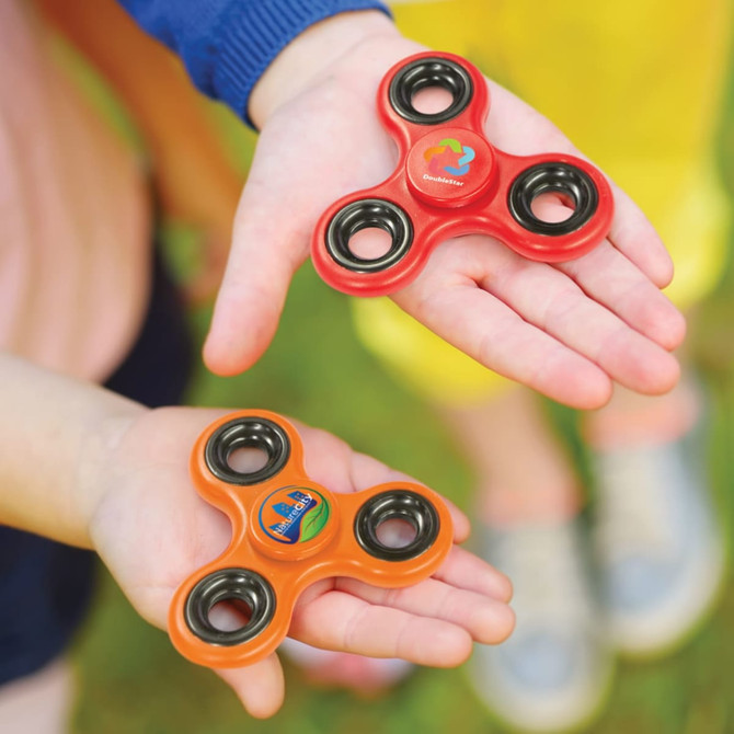 Two fidget spinners in vibrant colors—one red with a logo and the other orange with a different logo—held in hands.