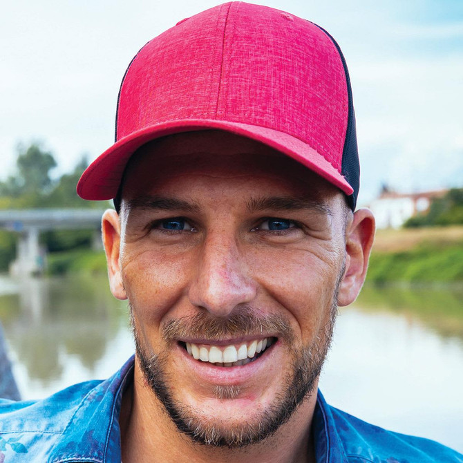 A cap featuring a red front and black mesh backing, set against a blurred outdoor background.