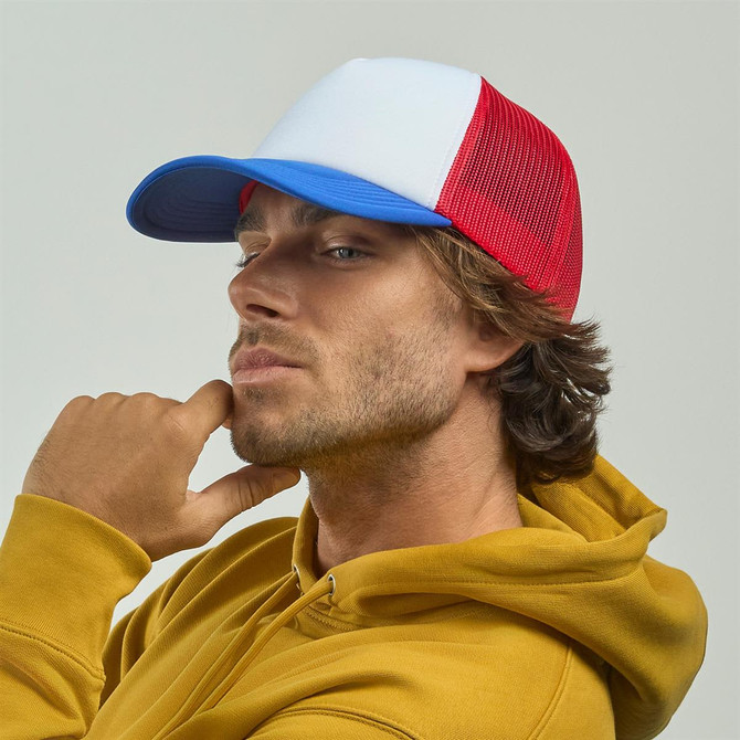 A man wearing a red and blue trucker cap, with a white front panel, poses thoughtfully in a yellow hoodie.