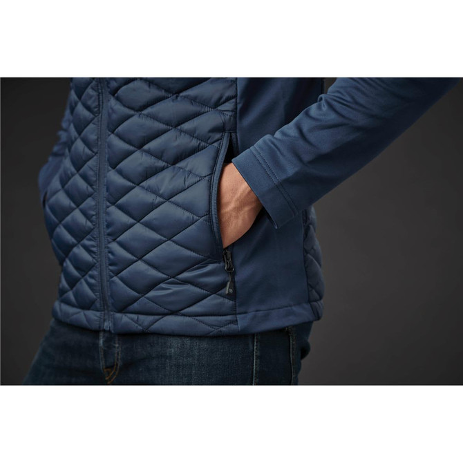 A men's thermal shell jacket in navy blue featuring a quilted design and side pockets. The model's hand is in a pocket.