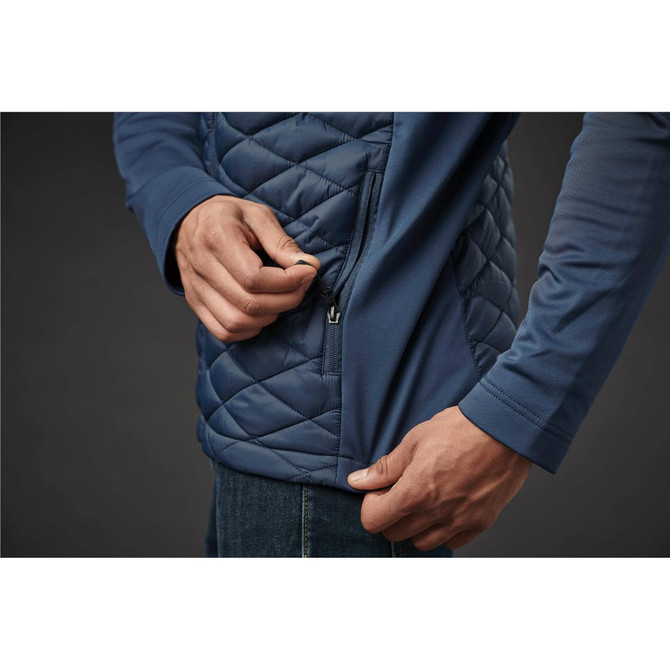 A close-up of a person adjusting the zip on a navy thermal shell jacket with a quilted design.