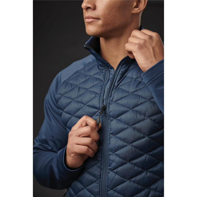 A man in a navy blue quilted thermal shell jacket, zipping it up, with a close-up on the jacket's detailing.