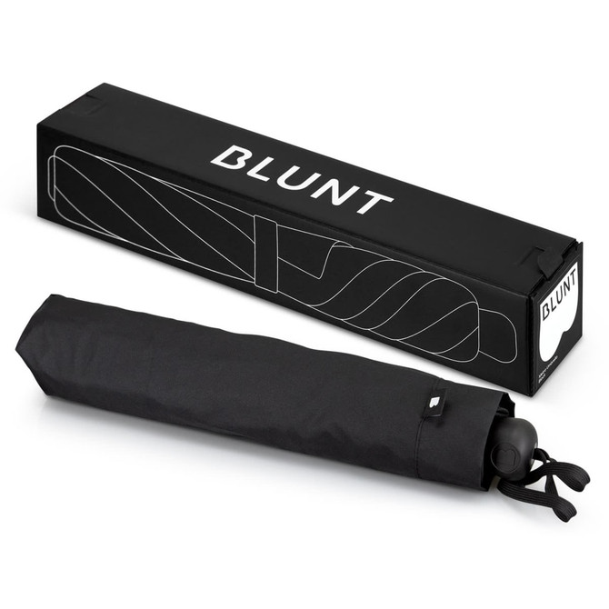 A black BLUNT Metro Umbrella laid flat next to its rectangular packaging, featuring a logo.