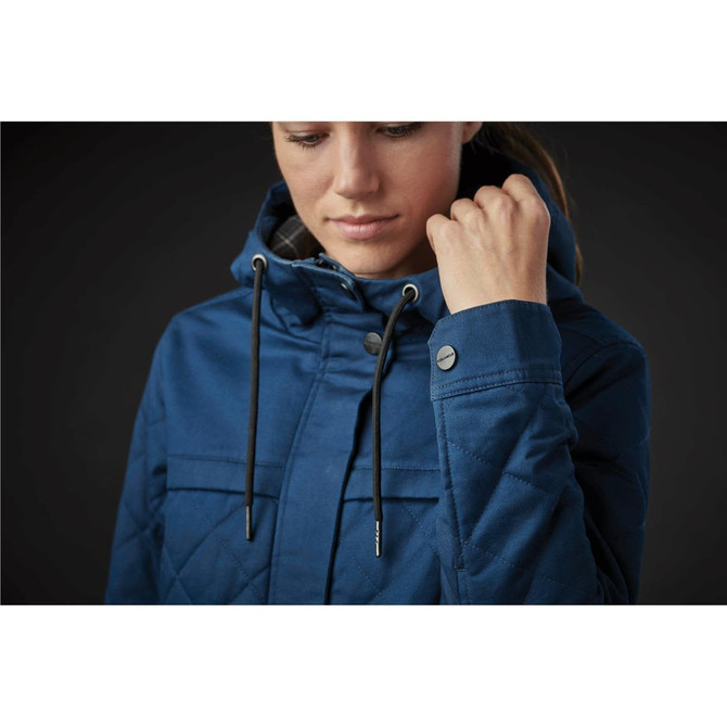 A woman wearing a blue quilted puffer jacket with a hood, featuring buttons and drawstrings.