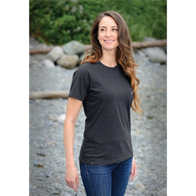 A dark grey women's t-shirt is displayed on a woman standing by rocky terrain, with trees in the background.