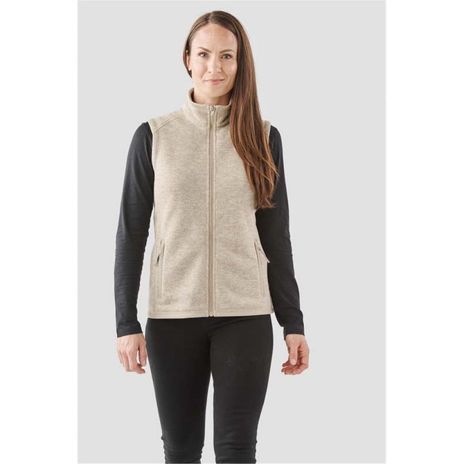 A woman is wearing a beige full zip fleece vest over a black long-sleeve top, featuring side pockets.