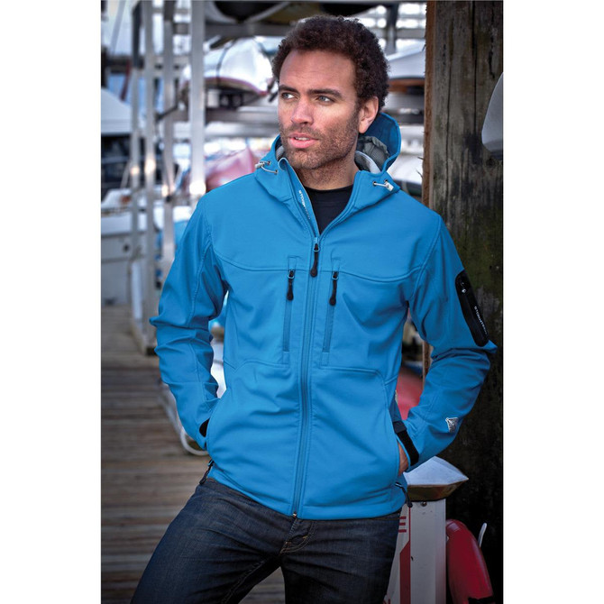 A blue men's jacket featuring a hood, zippered pockets, and a branding logo, worn by a model by the water.