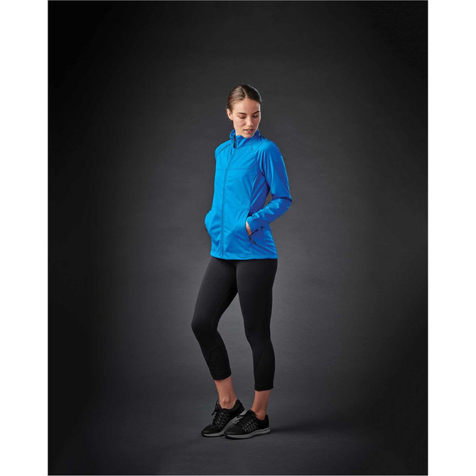 A woman wearing a bright blue lightweight softshell jacket with pockets, paired with black leggings and shoes.