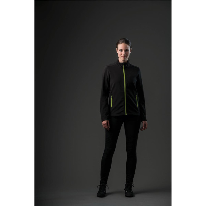 A woman wearing a black softshell jacket with bright green zippers and accents, set against a dark background.