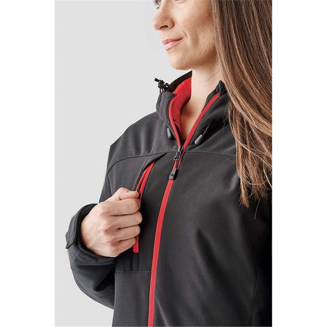 A woman models a black and red insulated softshell jacket with a zipper and hood. The jacket has a subtle logo.