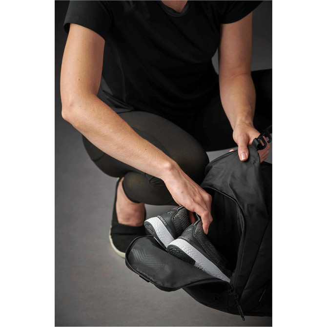 A person reaching into a black duffle bag, revealing a compartment for shoes or sneakers.