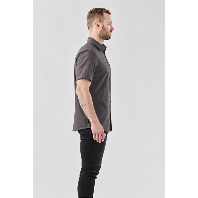 A grey short-sleeved button-up shirt worn by a man, featuring a subtle pattern. The shirt has a logo.