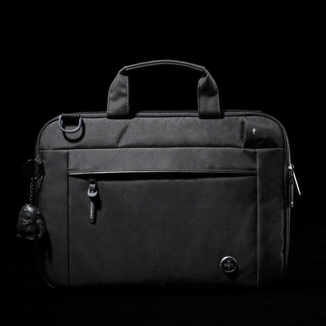 A black laptop sleeve with a zippered front pocket, handle, and a keychain accessory. It features a logo.