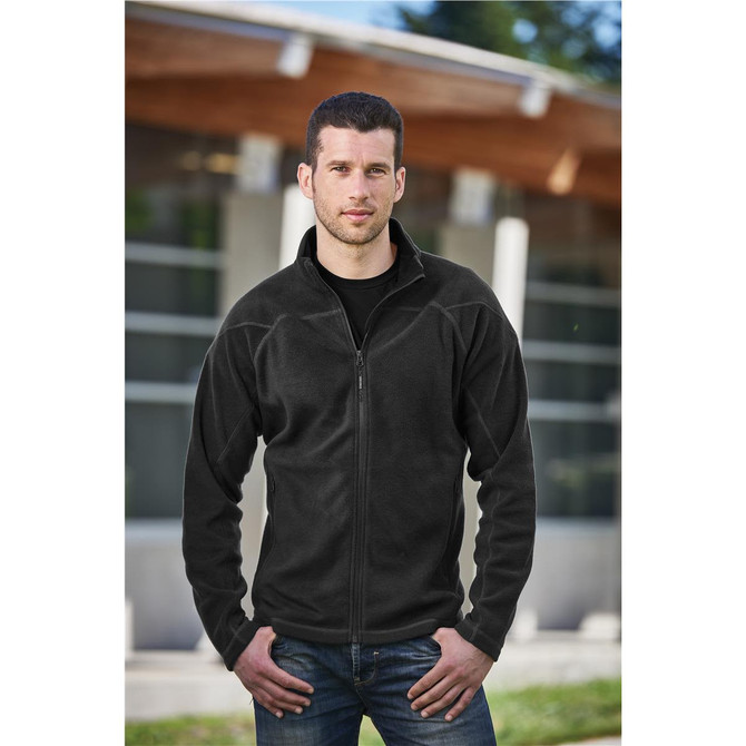 A man wearing a black polar fleece jacket with a full front zip, standing outdoors. The jacket features a logo.