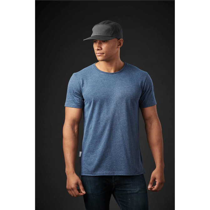 A men's crew neck T-shirt in blue, paired with a black cap, displayed on a model against a dark background.