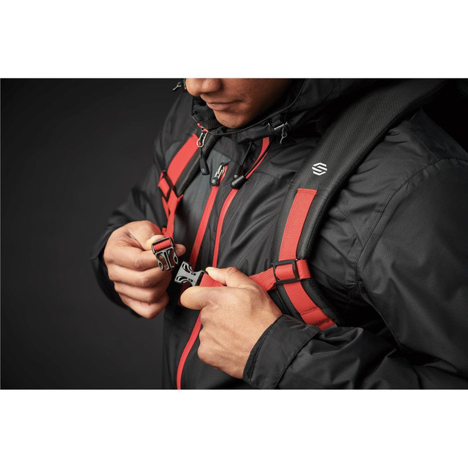 A person securing the straps of a black backpack with red accents, featuring a logo and a detailed harness system.