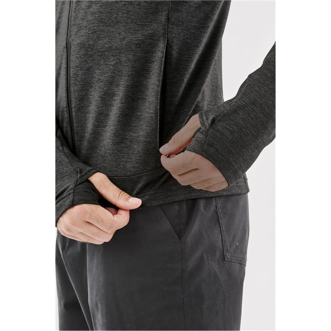 A close-up of a person adjusting the hem of a dark grey performance jacket. It features thumbholes in the sleeves.
