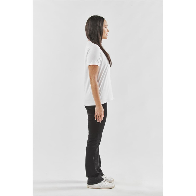 A side view of a female model wearing a white t-shirt and black pants, with casual white shoes.
