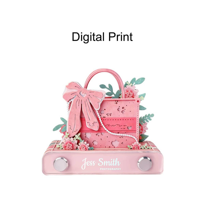 A pink 3D paper art handbag notepad, embellished with flowers and a bow, resting on a flat base with a logo.