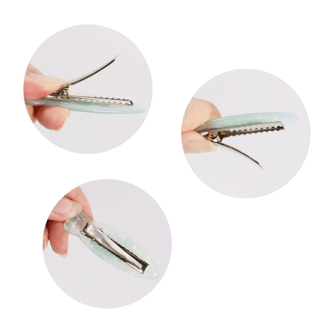 A fish-shaped iridescent hair clip in shades of green and blue held between fingers, showcasing its design and metal clasp.