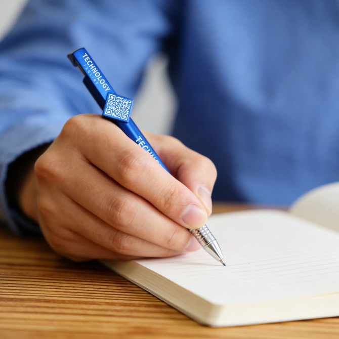 A blue pen with a QR code feature is being used to write in a notebook. The pen has a branding logo.
