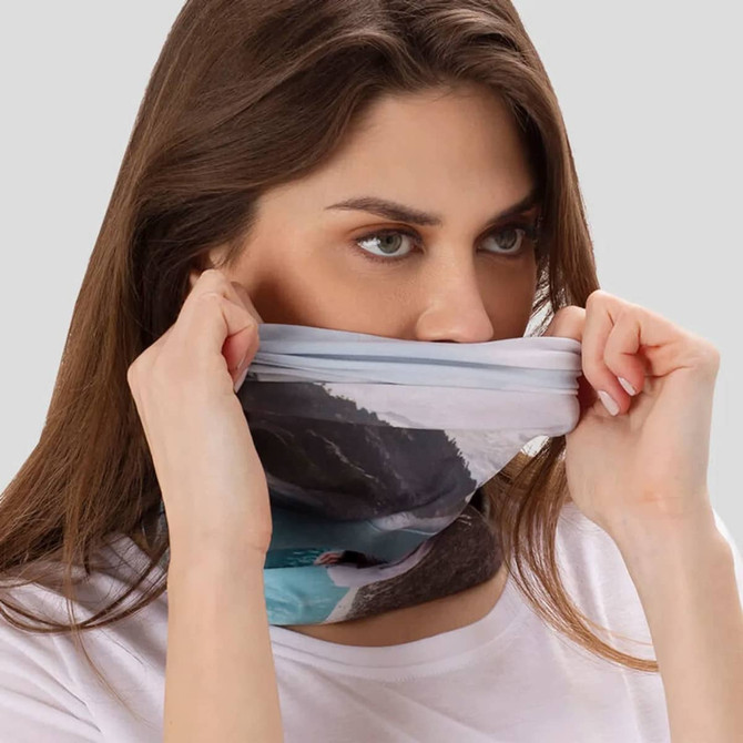 A large tubular bandana in shades of blue and grey, being worn around a woman's neck. It features a scenic design.