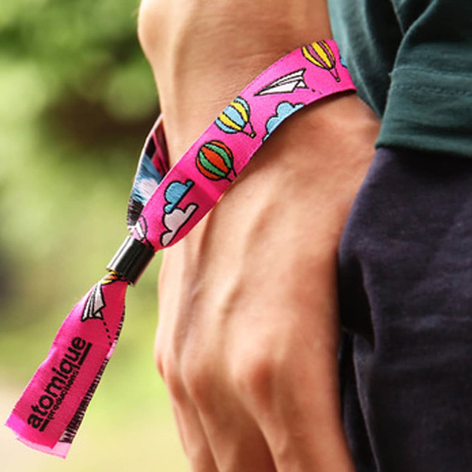 A pink wristband featuring colourful designs of balloons and paper planes, secured on a person's wrist.