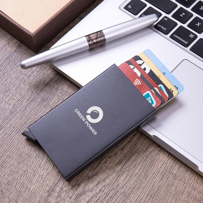 A sleek black metal RFID card holder displaying multiple cards, situated next to a laptop and a silver pen.