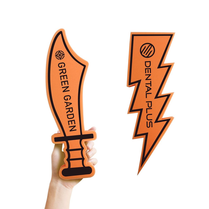 Two orange foam props are held in a hand: a sword shape labelled "GREEN GARDEN" and a lightning bolt labelled "DENTAL PLUS."