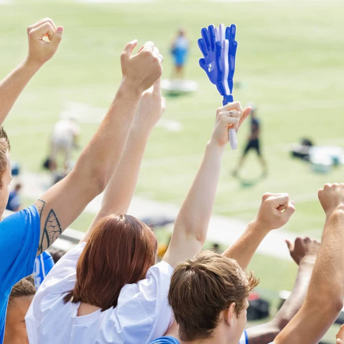 A pair of blue and white hand clappers held up among a crowd of cheering fans at a sporting event.